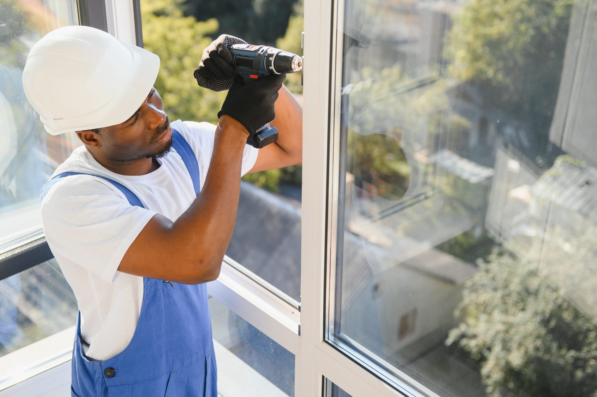Young African Repairman In Overalls Installing Window